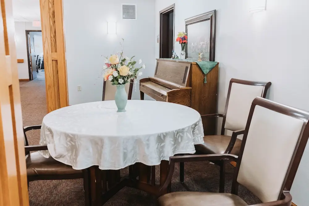 Round dining table with fresh flowers beside a piano at French Meadow Place